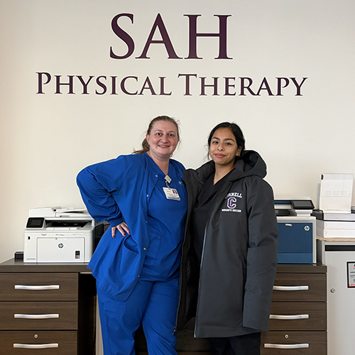 Student and alumna mentor standing in front of Saint Anthony Hospital logo in outpatient office.