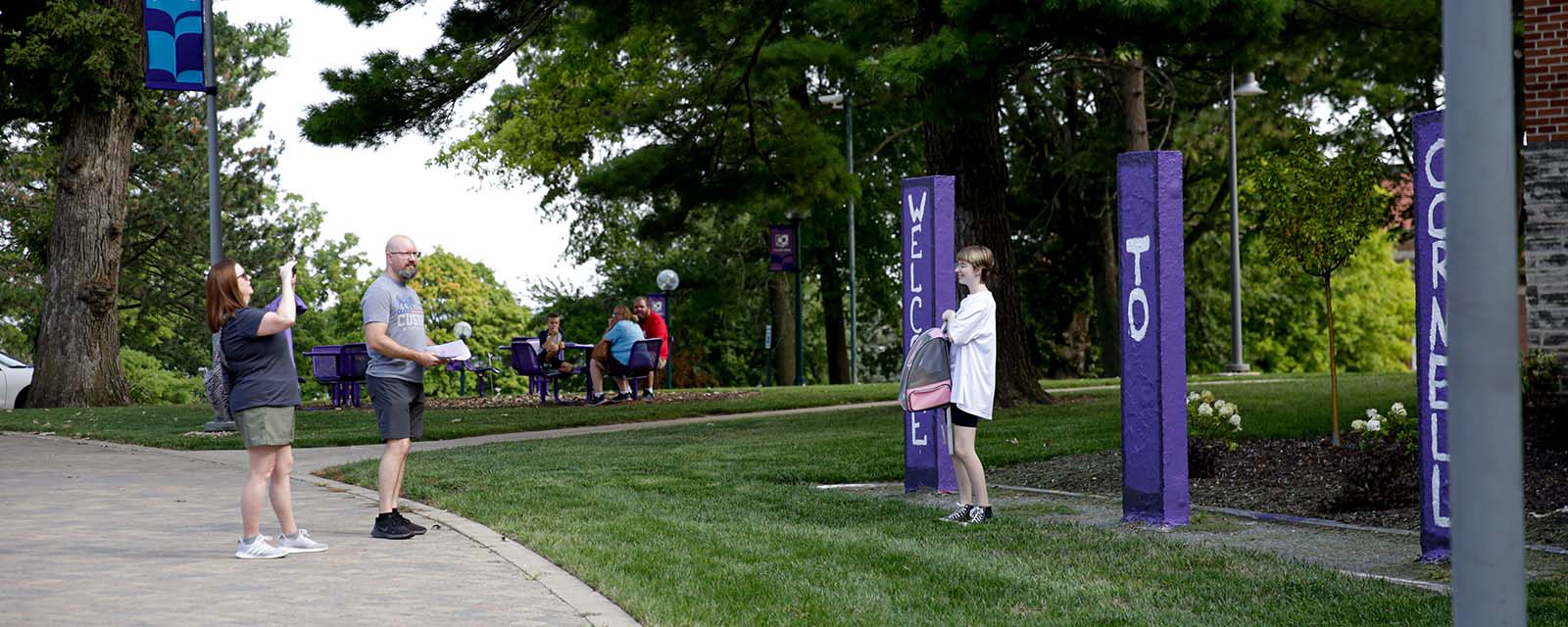 Parents taking a photo of their student in front of campus kiosks with welcome message.