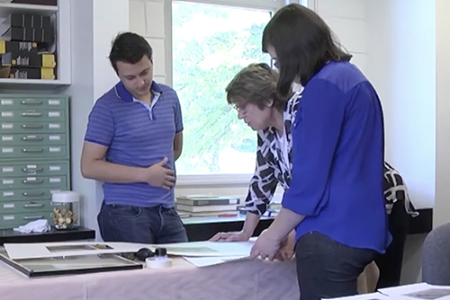 Professor and two students examine art in the archives