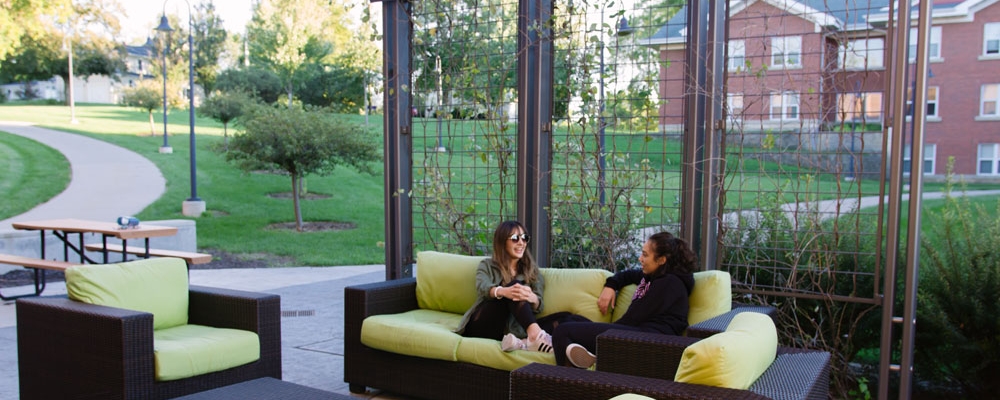 Two students sit on a couch on an outside patio near name hall.